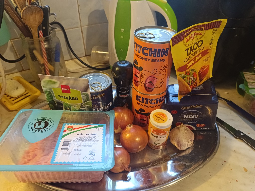 Ingredients pictured: ground pork, canned beans, canned tomatoes, oregano, onions, garlic, taco seasoning, pepper, cumin, tomato sauce